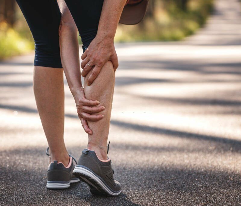 a person wearing sports clothes and sneakers holding their leg on a road