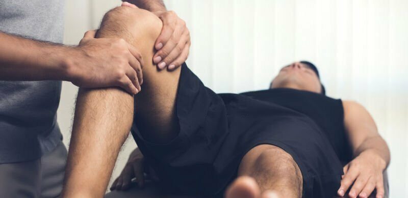 a person lying on a bed with his leg in the air while a doctor examines it.